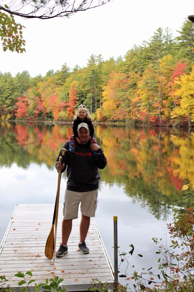 Dad and daughter posing on the doc on the water with beautiful fall foliage